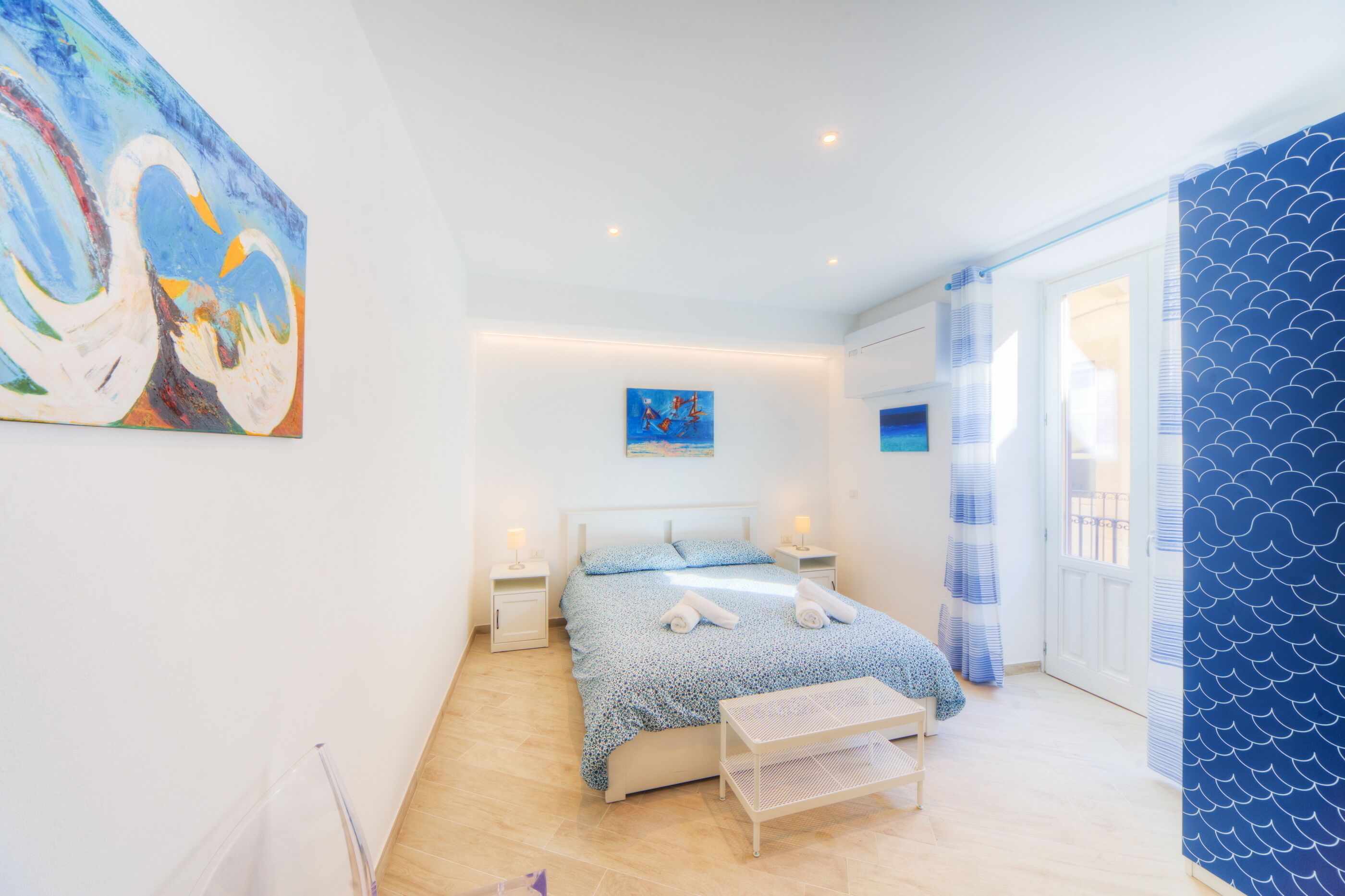 A modern bedroom with a bed, bedside tables, and artwork on the walls.