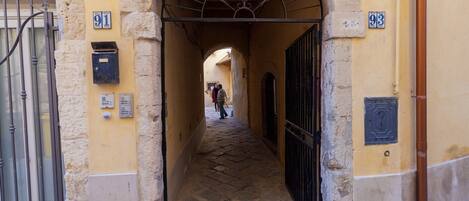A narrow alleyway with stone walls and arched doorways, leading to a building with numbered doors.