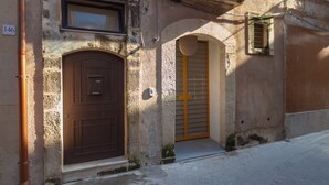A two-story building with a brown door, a small balcony with a metal railing, and a window above the door.