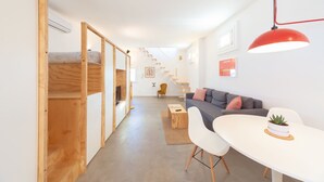 A modern living space with a bunk bed, a sofa, a dining table, and a staircase leading to an upper level.
