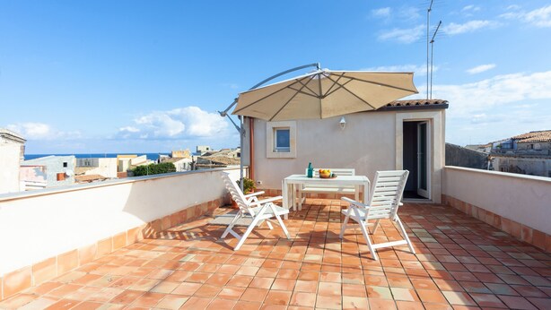 A rooftop terrace with a table and chairs, a large umbrella, and a view of the city.