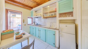 Een keuken met blauwgroene kastjes, een witte koelkast en een raam met uitzicht op buiten.