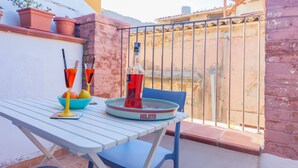 Een tafel met een fles Mojito, glazen en een schaal fruit op een balkon, met uitzicht op een gebouw en een poort.