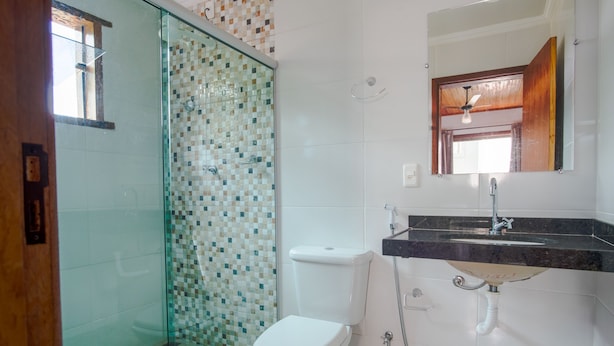 A bathroom with a glass shower enclosure, a toilet, a sink with a mirror above it, and tiled walls. - Pousada Topo do Cipó (Santana do Riacho)