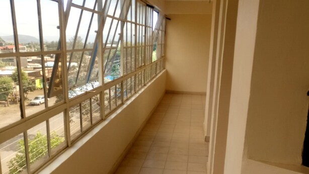 A corridor with tiled flooring, a window with metal bars, and a view of the outside. - Club Settlers (Nakuru)