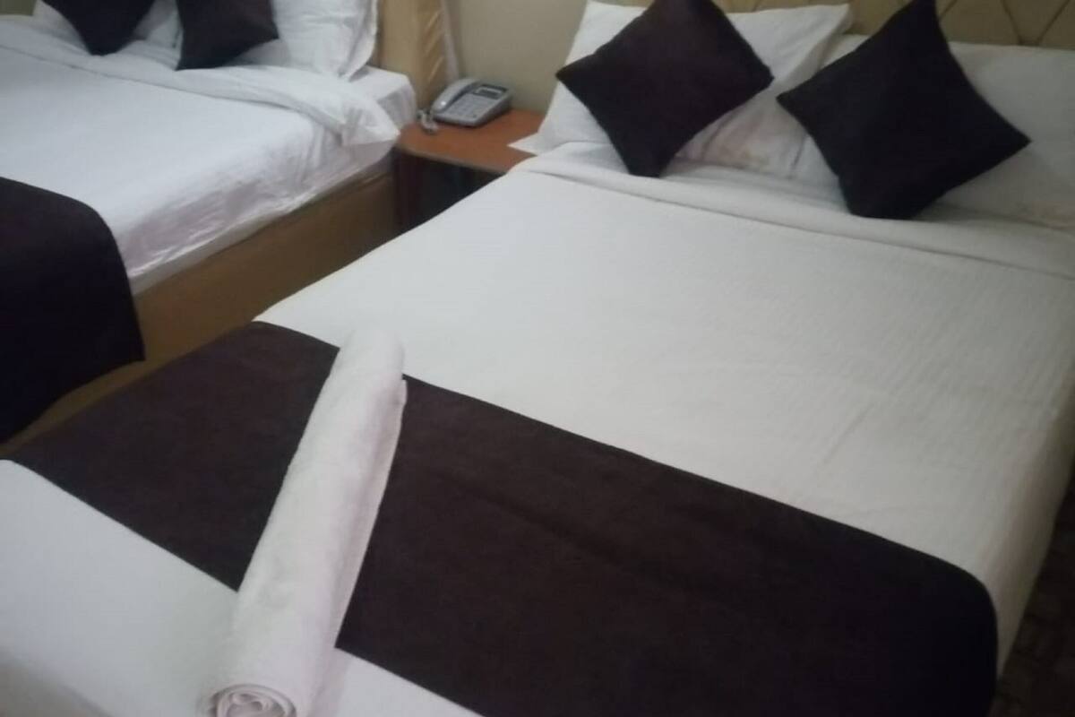 A hotel room with two beds, each with white linens and dark brown headboards. There is a small bedside table with a telephone on it.