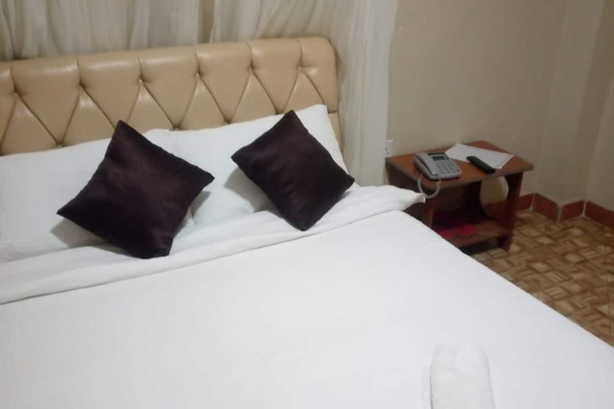 A bed with a tufted headboard, white linens, and two dark pillows. A bedside table with a telephone and a notepad is visible.