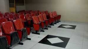 Une rangée de chaises rouges à assise noire, disposées dans un espace d’attente doté d’un sol carrelé et d’une porte en arrière-plan.