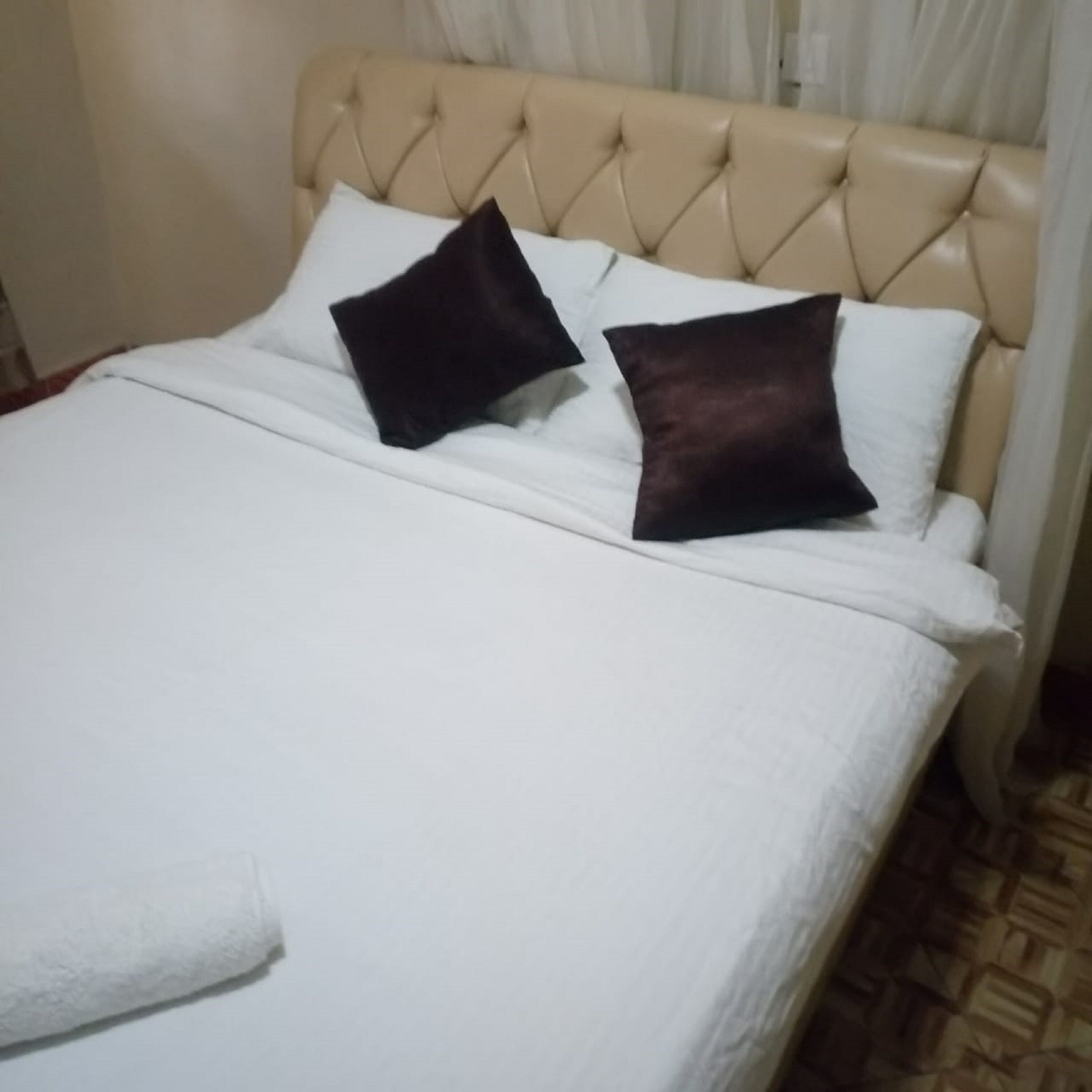 Una cama con cabecera capitonada, ropa de cama blanca y dos almohadas oscuras.