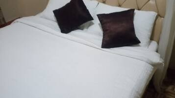 Una cama con cabecera capitonada, ropa de cama blanca y dos almohadas oscuras.