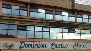 La façade extérieure de l’hôtel Dominion Castle, avec son espace d’accueil, une voiture garée et un pot de fleurs.