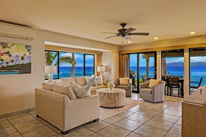 A living room with a view of the ocean, a ceiling fan, and a dining area with a table and chairs.