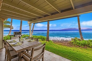 A covered outdoor dining area with a view of the ocean and a grill.