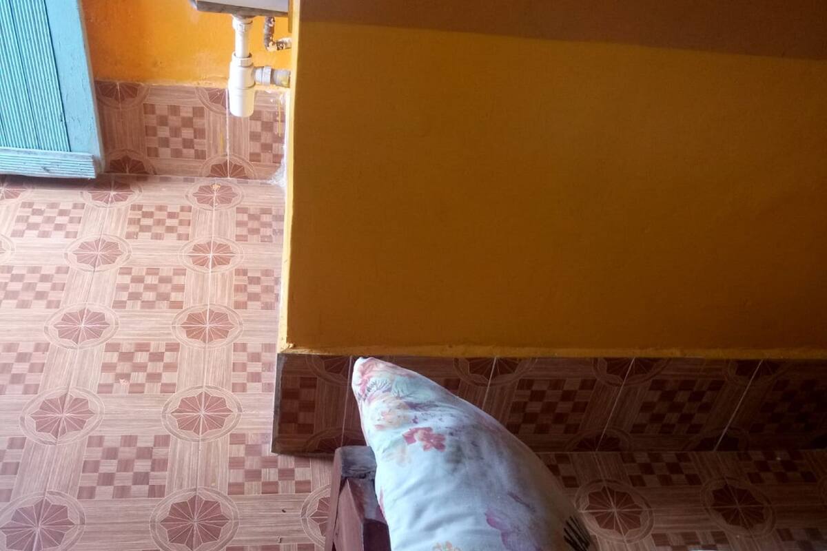 A room with a patterned floor, a bed with a floral pillow, and a yellow wall.