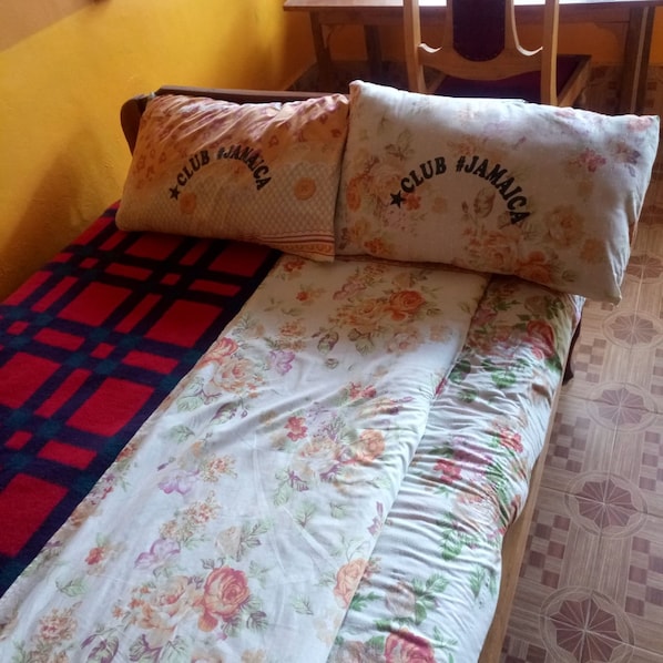 A bed with floral bedding and two pillows with 'CLUB JAMAICA' text, a red and black checkered blanket, and a patterned floor.