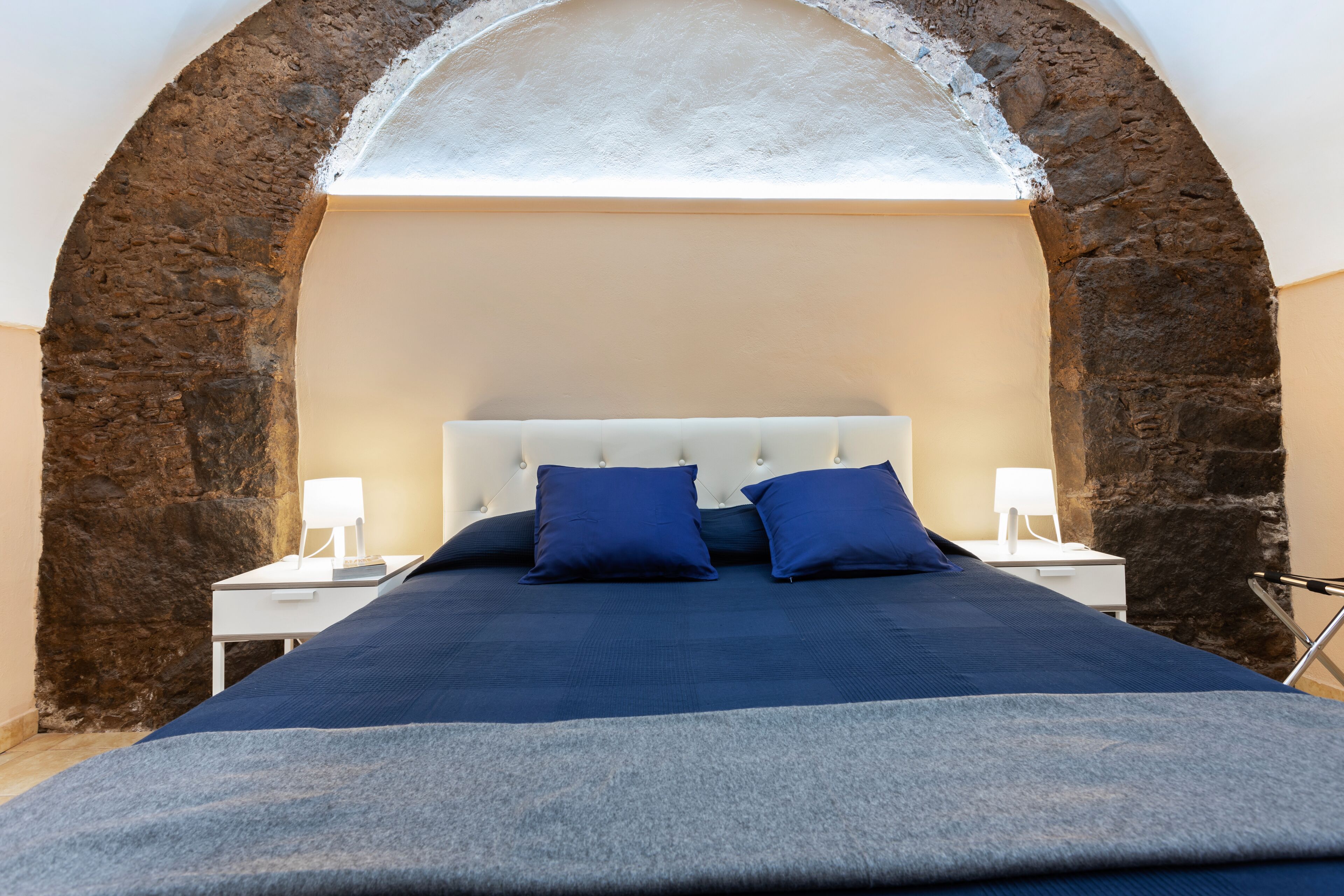 Un dormitorio con un arco de piedra, una cama con ropa de cama azul y lámparas de noche.