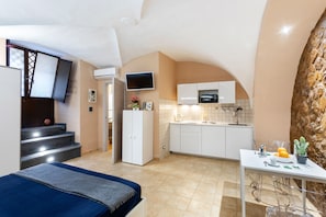 Camera d'albergo compatta con un letto, un angolo cottura, una TV a parete e una scala che conduce a un livello superiore.