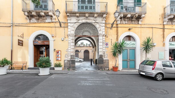 Une vue de rue avec un bâtiment doté d’une entrée en arc de cercle, de plantes en pot et de voitures garées.