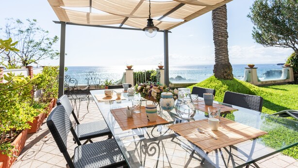 Une terrasse extérieure avec une table en verre, des chaises et une vue sur la mer.