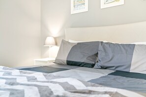 Una cama bien hecha con una colcha estampada, cabecera blanca y una lámpara de noche.