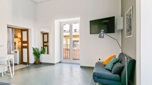 Ein modernes Wohnzimmer mit einer Couch, einem Fernseher und einer Lampe. Eine Tür führt zu einem Balkon.