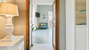 Ein Flur, der in ein Wohnzimmer mit einer Couch, einer Lampe und einem an der Wand befestigten Fernseher führt.
