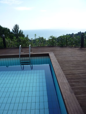 A swimming pool with a wooden deck and a view of the sea.