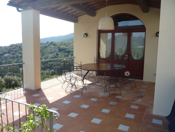 A balcony with a table and chairs, a view of the surrounding landscape, and a door with glass panels.
