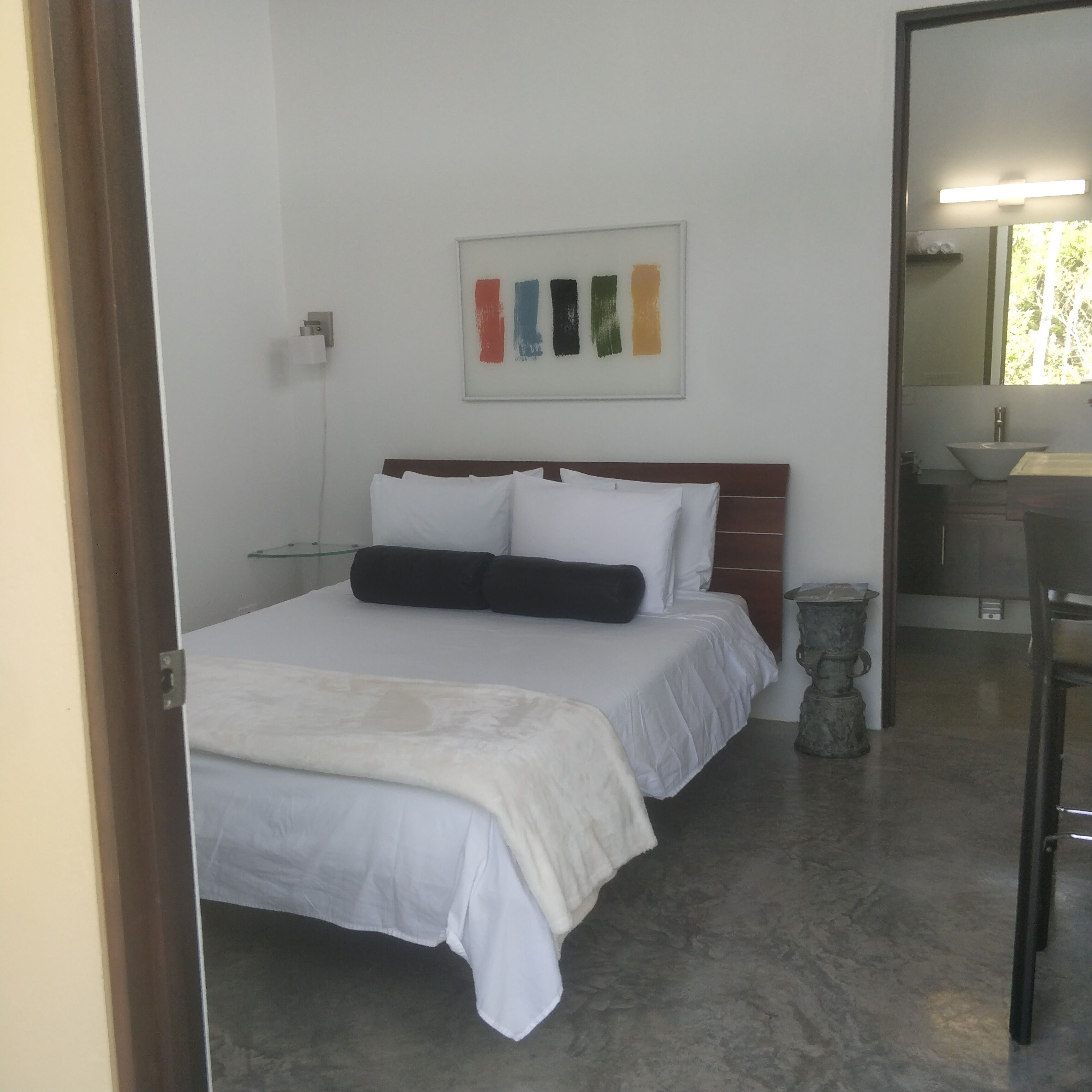 Une chambre à coucher comprenant un lit, une table de chevet, une commode, un miroir et une salle de bain visible à travers une porte ouverte.