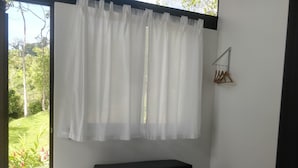 A bedroom with a bed, a bench, and a view of greenery outside.