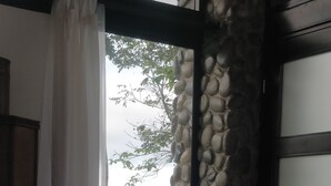 A room with a stone wall, a view of greenery and hills, and a partially open door with a curtain.