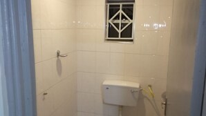 A small, tiled bathroom with a toilet, a window, and a showerhead. - Kape Samaritan Guest House (Makutano)