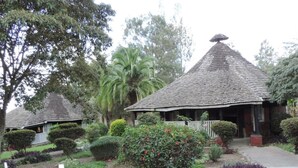 A traditional thatched-roof structure surrounded by well-maintained gardens. - Lions Court Lodge (Nanyuki)