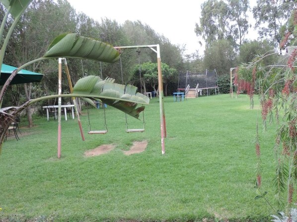 A grassy backyard with a swing set and a covered seating area.
