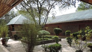 A courtyard with potted plants, a stone building, and a wooden pergola. - Lions Court Lodge (Nanyuki)
