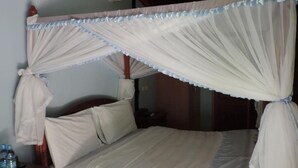 A bed with a canopy, pillows, and a nightstand with water bottles. - Lions Court Lodge (Nanyuki)