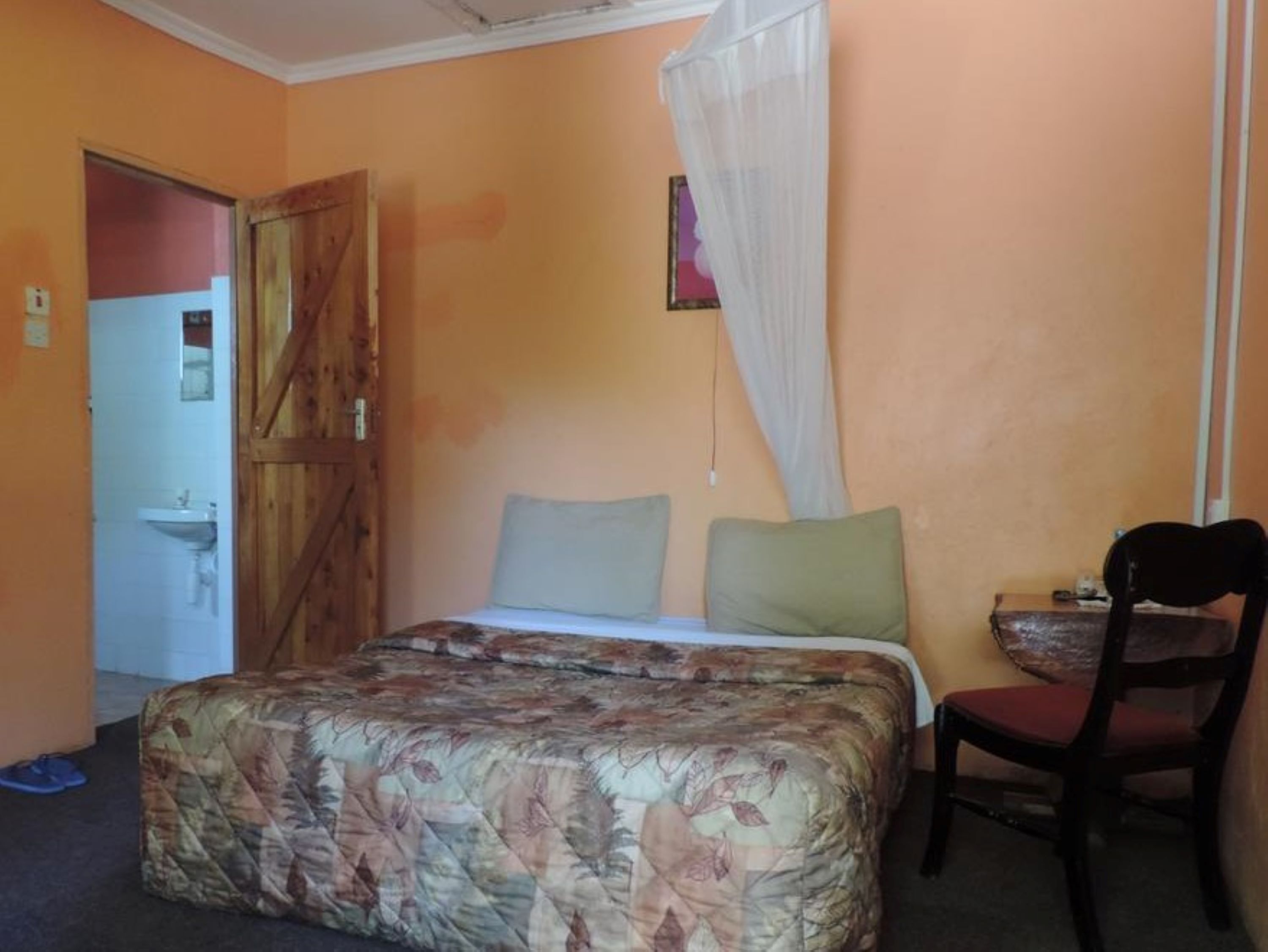 A bedroom with a bed, a chair, a bedside table, a window with a curtain, and a door leading to a bathroom.
