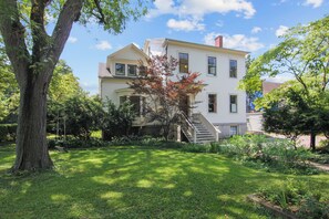 A two-story house with a front yard, a staircase leading to the entrance, and a large tree in the foreground.