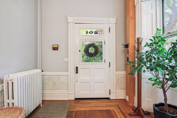 A white door with a wreath, a small sign above it, and a potted plant to the right.