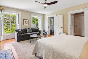 A bedroom with a large bed, a dark-colored sofa, a coffee table, and a ceiling fan.