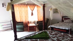 A bedroom with a canopy bed, a small table, two chairs, and a view of the outside through curtains. - Mseven Gardens M7 (Nyahururu)