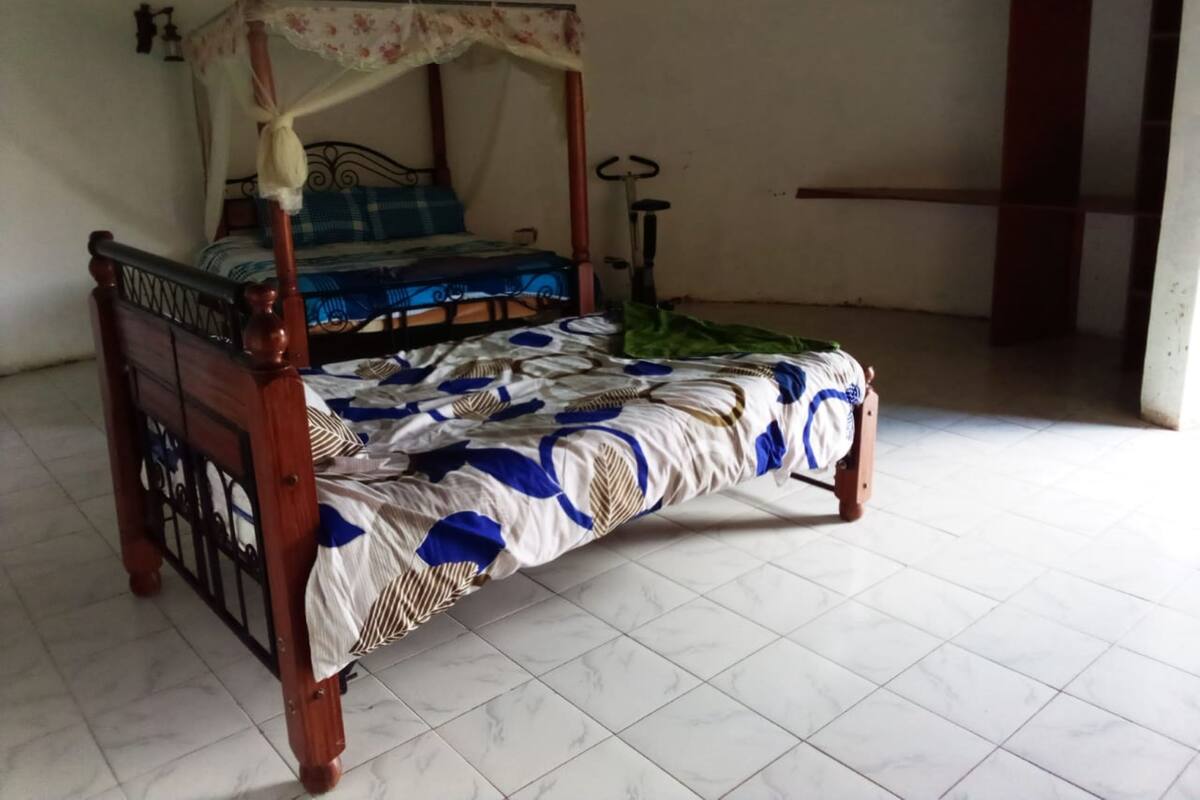 A four-poster bed with a floral canopy, a blue and white patterned bedspread, and a green blanket on the floor.