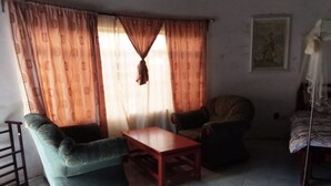 A living room with a sofa, two armchairs, a wooden coffee table, and a bed with a patterned bedspread. - Mseven Gardens M7 (Nyahururu)