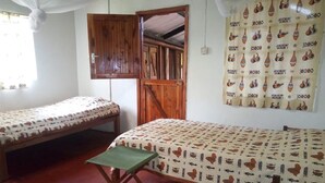 A room with two beds, one with a green bench, wooden doors, and a patterned curtain. - Muremba Retreat Kitale (Kitale)