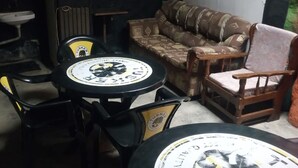 A room with a green wall, a brown patterned sofa, a wooden chair, a small table, and a black chair with a yellow logo. - Mwaki-Mugi Hotel & Campsite (Nakuru)