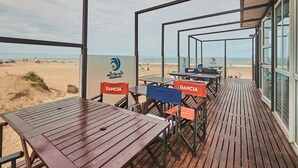 Un espacio de estar al aire libre con mesas y sillas de madera, vista al mar y un logotipo en la pared.