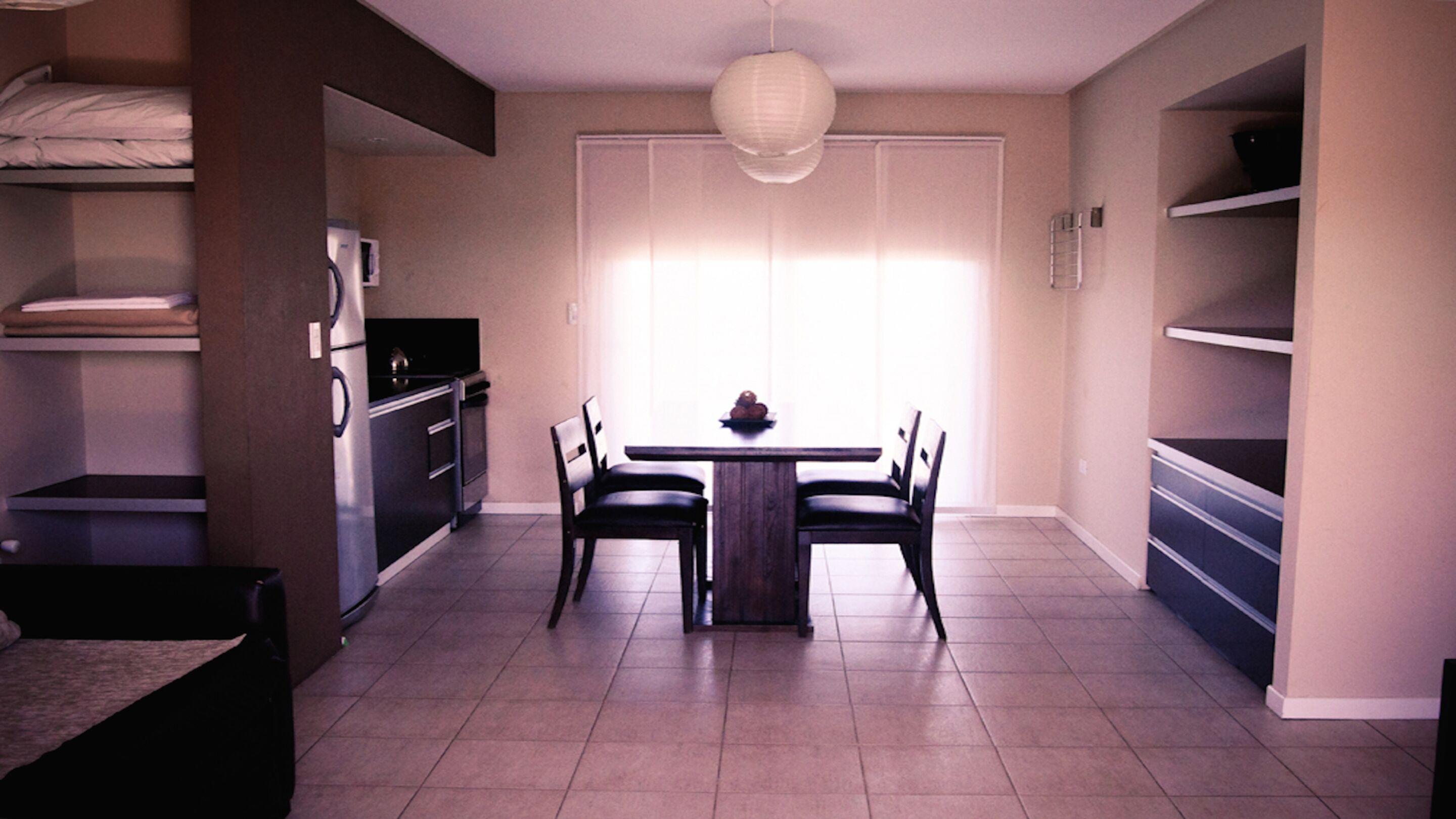 Un espacio habitable compacto con kitchenette, una zona de comedor con mesa y sillas, y un ventanal que proporciona luz natural.