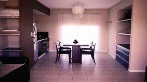 Un espacio habitable compacto con kitchenette, una zona de comedor con mesa y sillas, y un ventanal que proporciona luz natural.
