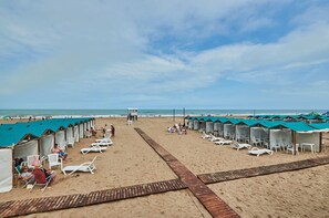 Una playa con hileras de cabañas de playa y tumbonas, un paseo de madera y el océano al fondo.