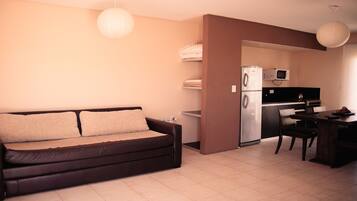 Un espacio habitable compacto con sofá, mesa de comedor, zona de cocina con refrigerador y microondas, y televisor.
